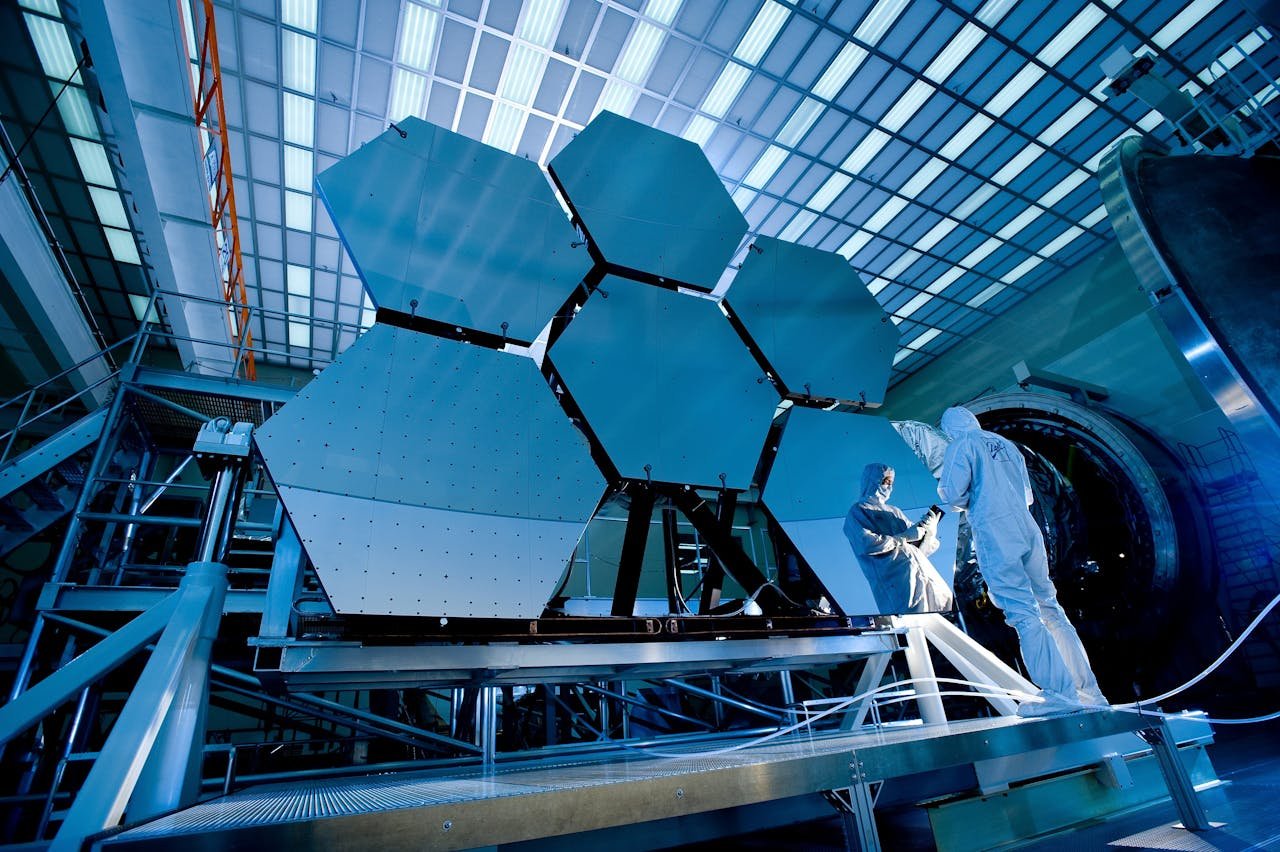 About Engineers in protective suits work on telescopic mirrors in a high-tech lab.