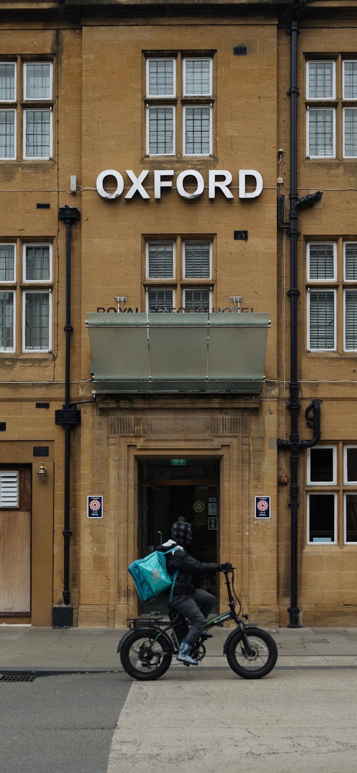 Offerings Biker passing in front of Oxford building with classic architecture.