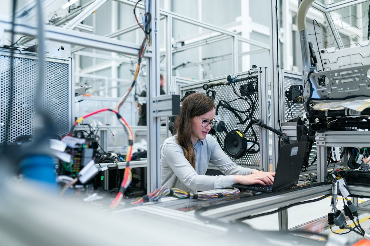 About A female engineer focuses on her laptop amidst advanced tech equipment in a lab.