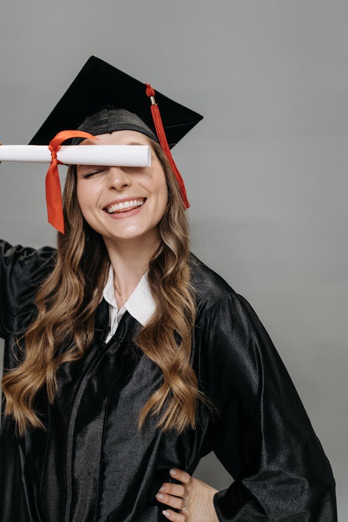 Smiling woman in graduation gown celebrating with diploma in hand indoors.